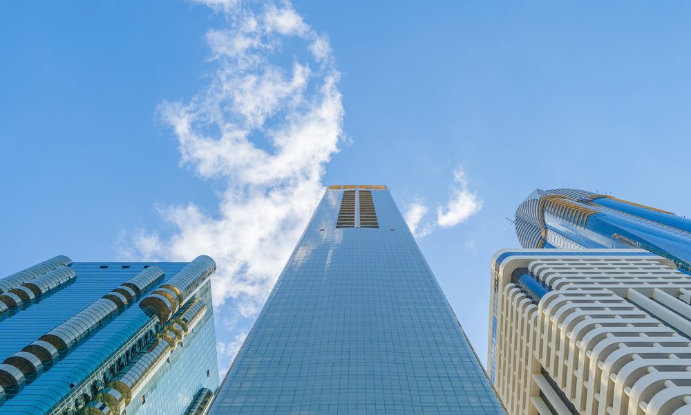 Looking up to high-rise office buildings, skyscrapers, architectures in financial district with blue sky. Smart urban city for business and technology concept background in Downtown Dubai, UAE.